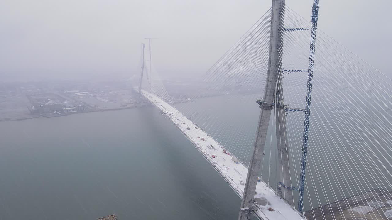 Aerial view of Gordie Howe Bridge disappearing into dense winter mist over Detroit River
