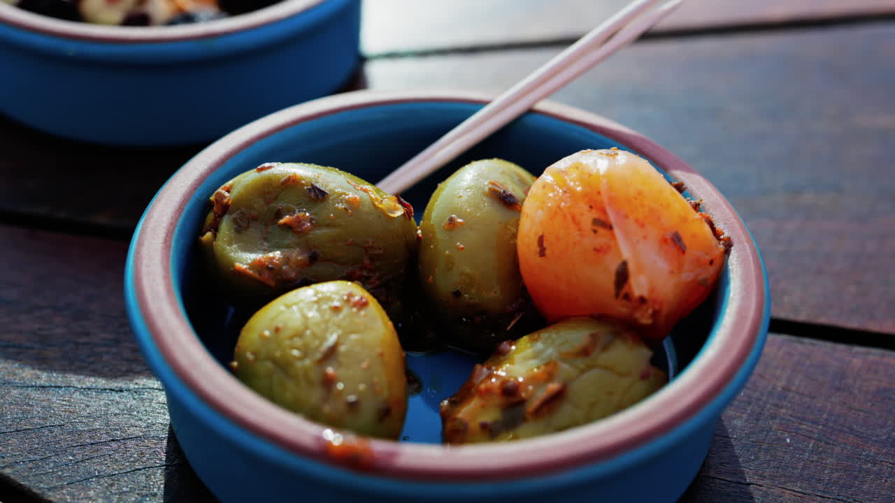 Close up of a hand picking up a green olive with a toothpick on a small bowl on a table