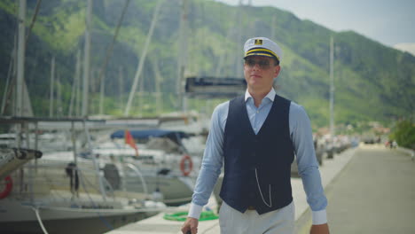 man in a captain's hat walking along a dock by yachts