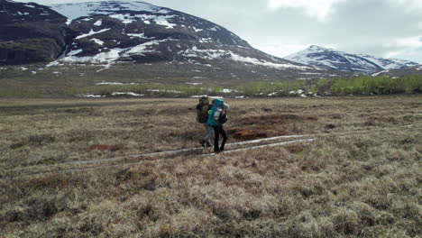young couple hiking on the kungsleden in the abisko national park, lateral close drone shot of hikers in a serene mountain swedish landscape