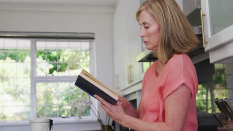 mujer caucásica de edad avanzada de pie en la cocina en casa leyendo un libro