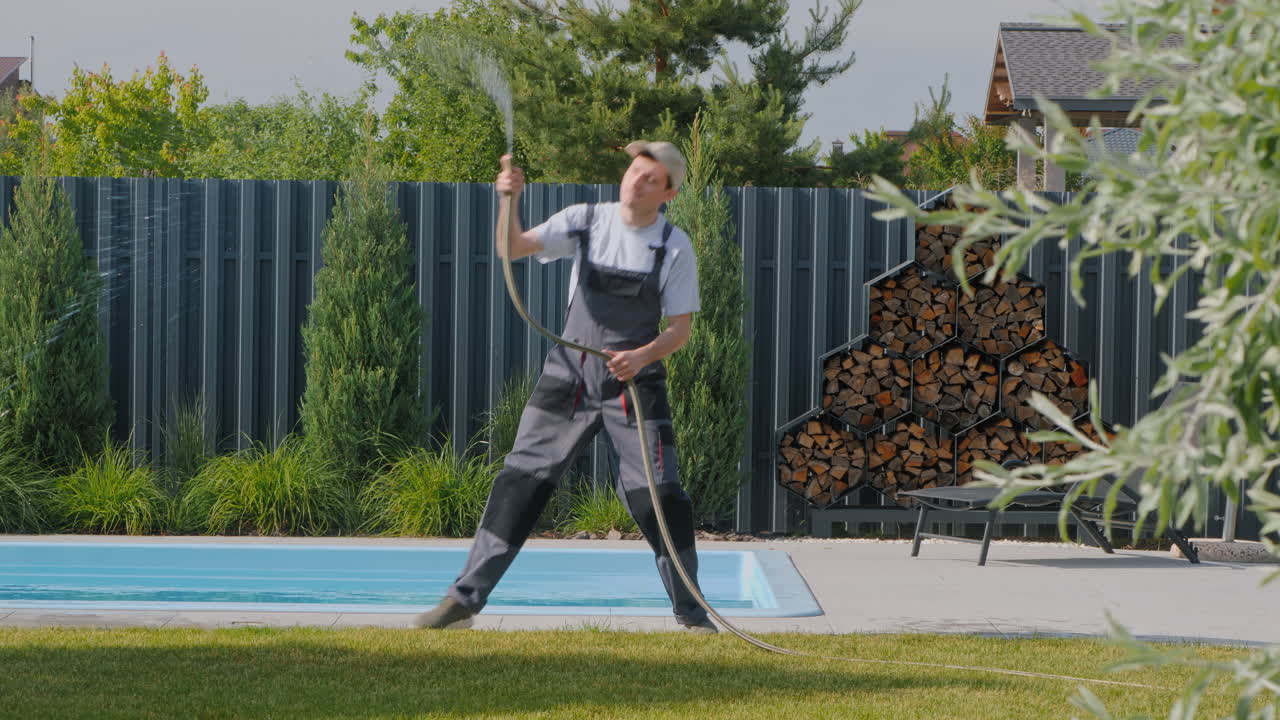 수영장 근처 에 있는 사람 이 정원 에 물 을 주고 있다