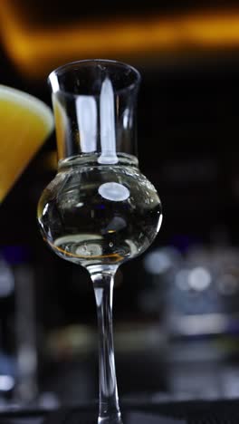 close up of a glass of liquor with cocktail in the background