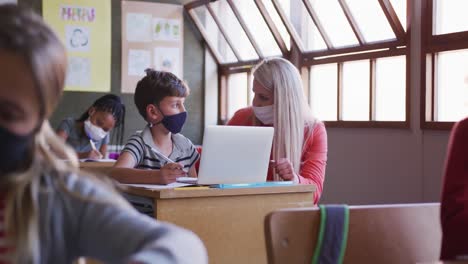 maestra y niño con máscara facial usando una computadora portátil en clase en la escuela