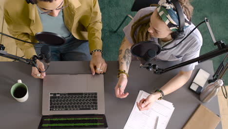 top view of young man and woman wearing headphones sitting at a table with microphones while they recording a podcast