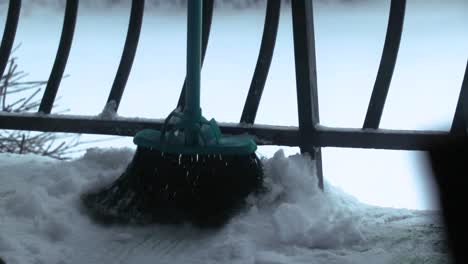 un primer plano de una escoba empujando la nieve desde un balcón