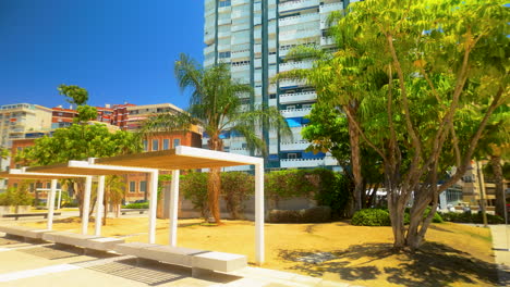 día soleado en la malagueta de málaga con asientos modernos y edificios altos cerca