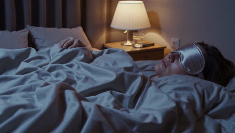 person sleeping peacefully in bed with a sleep mask at night