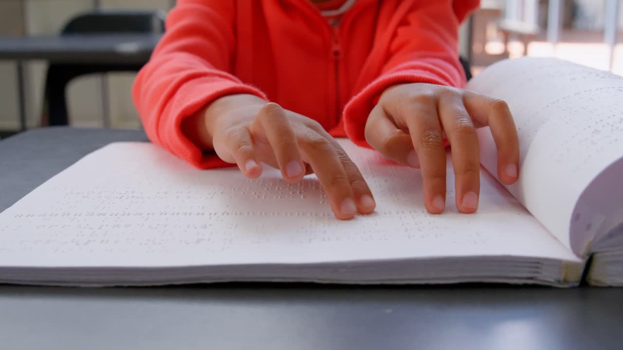 sección media de un escolar asiático ciego que lee un libro en braille en el aula de la escuela 4k