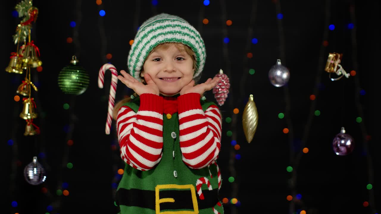 Holčička v kostýmu vánočního skřítka, pomocníka Santa Clause, si zakrývá obličej rukama a hraje si na schovávanou.