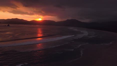 the stunning view of the sun setting behind the mountains and beach of java, indonesia - aerial shot