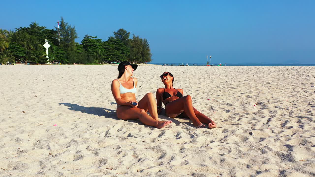 Smiling girls with tanned skin sunbathe on quiet sandy beach on tropical island with bright blue sky background in Philippines