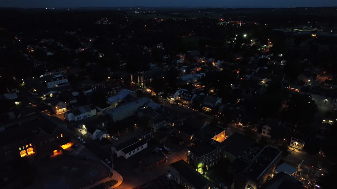 Centro città illuminato in America di notte. Lanterne con illuminazione calda lungo le strade. Case in un quartiere tranquillo. Ripresa aerea dall'alto. Traffico su Main Street.