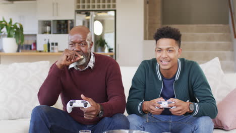 excited african american father and adult son playing video game and celebrating, slow motion