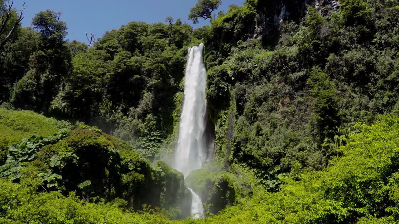 Handheld of Salto El Leon big waterfall falling into rocks covered in moss in dense rainforest near Pucon, Chile