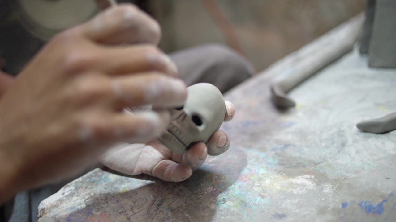 Closeup of artisan carving handmade clay skull for Catrina sculpture using metal tool to round edges and add structural details