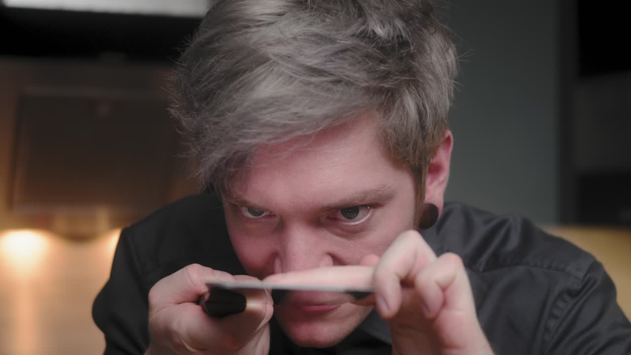 우아한 검은 셔츠를 입은 젊은 미친 사이코패스 남성 셰프가 칼을 자르고 칼날을 만지는 사악한 시선, 대안적인 외모와 문신을 새긴 현대적이고 멋진 부엌 슬로우 모 시네마틱 돌리