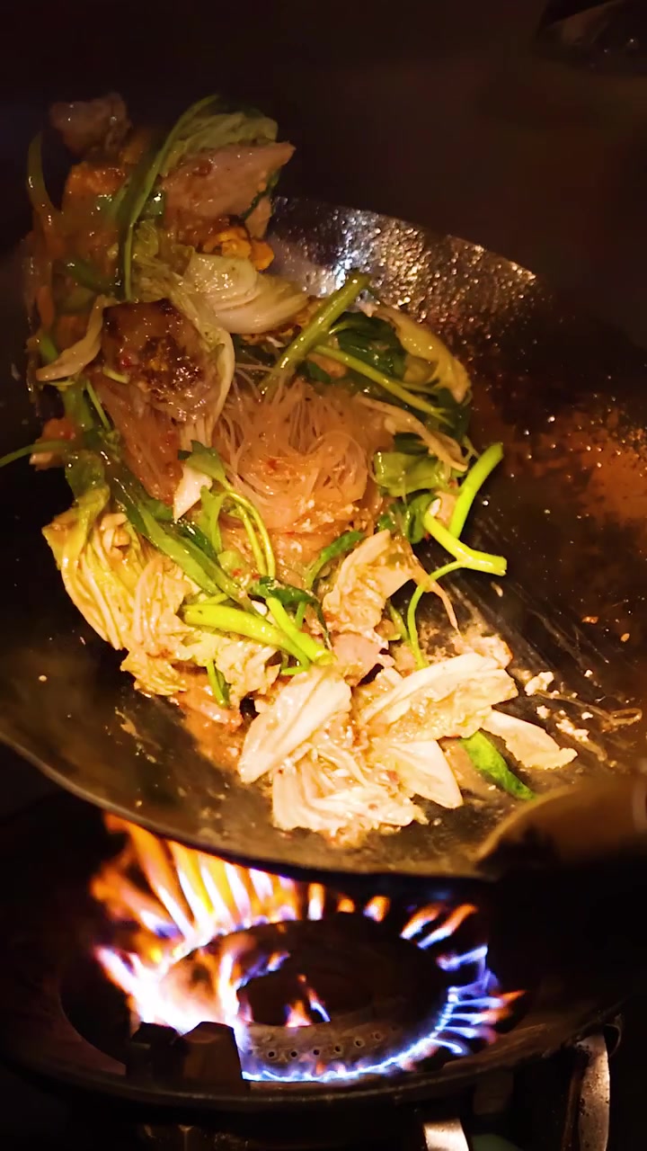Ein Koch brät energisch Suki-Yaki mit Gemüse in einem Wok über intensiver offener Flamme an.