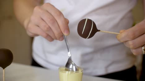 woman decorating dark chocolate cake pops with white chocolate making spirals