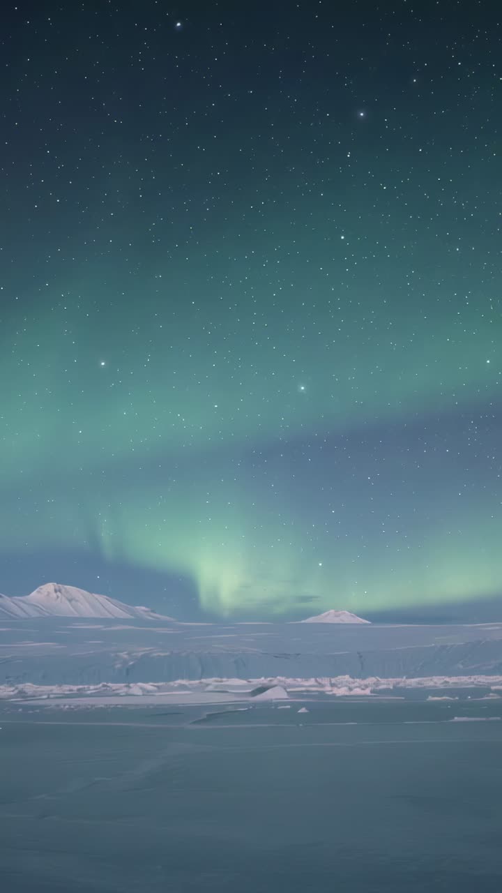 Vertical video: Brightening auroral band forming green curtain over frozen sea, mountains, stars