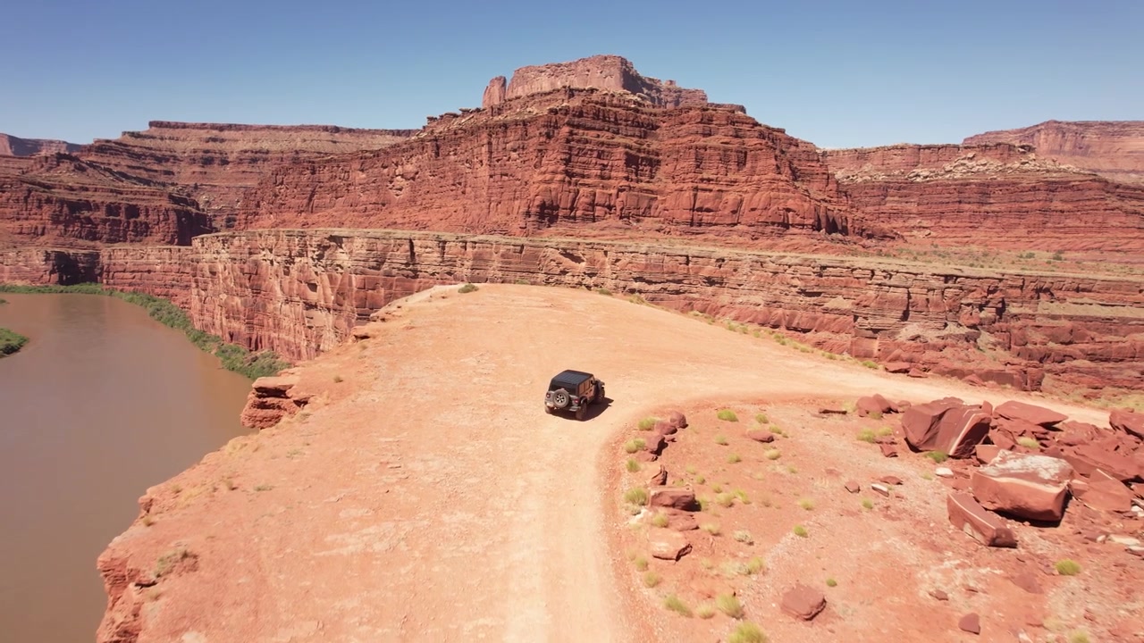 Drone che segue un fuoristrada che guida vicino a una scogliera tra le montagne di roccia rossa di Moab, USA, in 4k