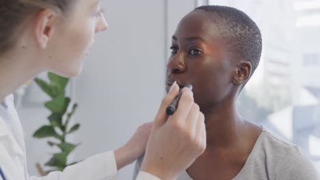 diverse female patient and doctor, inspecting her eye with penlight in hospital, in slow motion