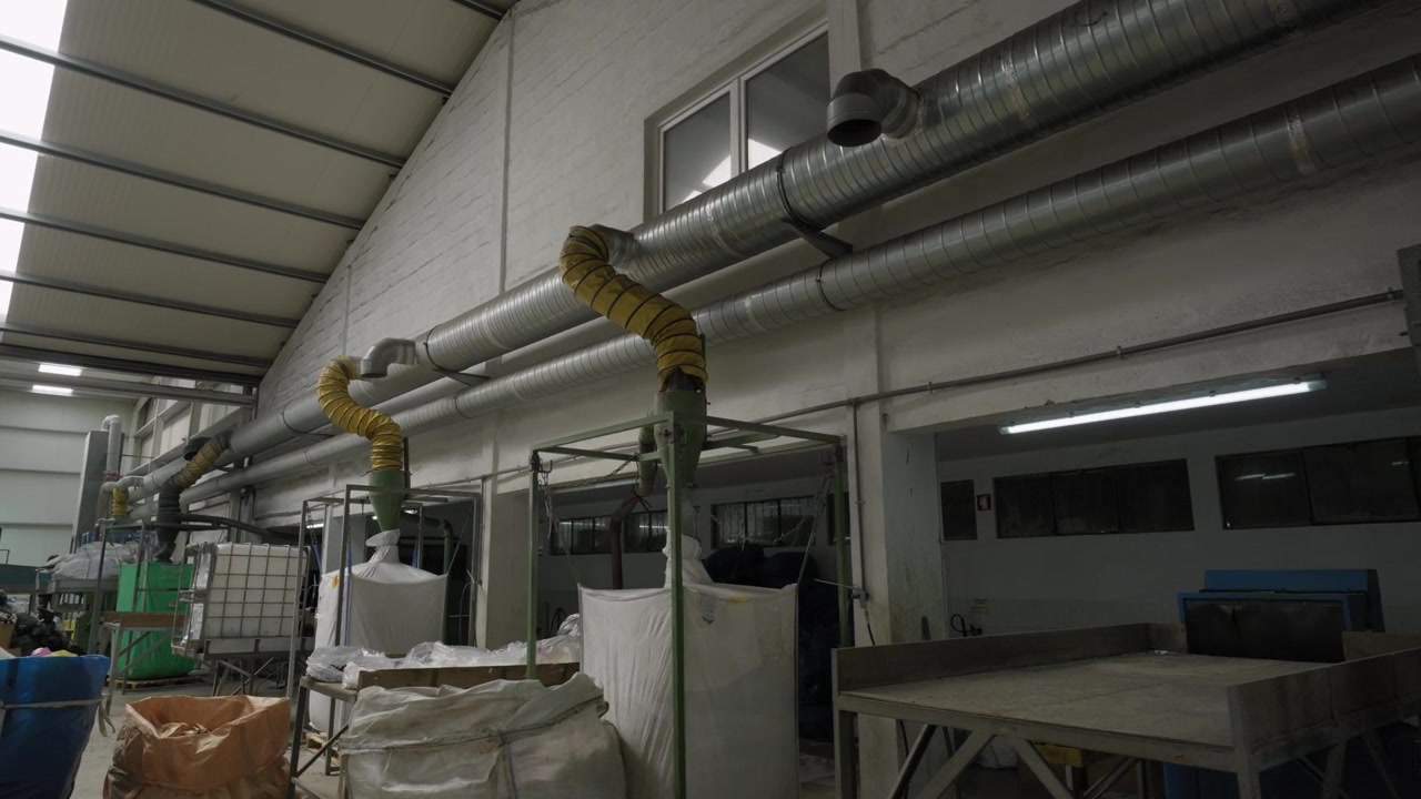 Metal ductwork and flexible pipes run along the ceiling of a plastic recycling factory interior