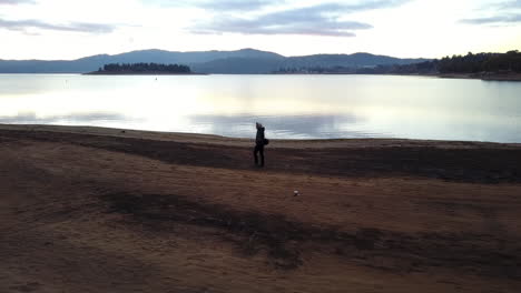 Silhouette-Einer-Person,-Die-Am-Goldenen-Sandstrand-Des-Lake-Jindabyne,-New-South-Wales,-Australien,-Spazieren-Geht