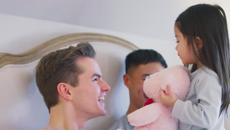 familia con dos padres en la cama en casa jugando con su hija y su juguete blando
