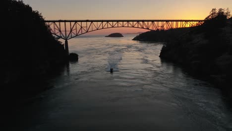 Aerial-view-of-a-motorboat-traveling-under-Deception-Pass-at-sunset-on-a-warm-summer-evening