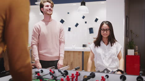 young business creatives playing table football together at work celebrate a goal, close up