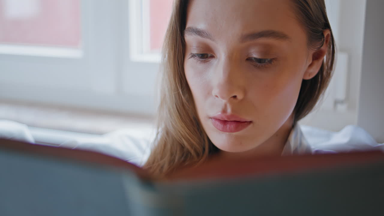 Primo piano di una donna che legge un libro seduta sul letto di casa. Donna pensierosa e concentrata sulla lettura