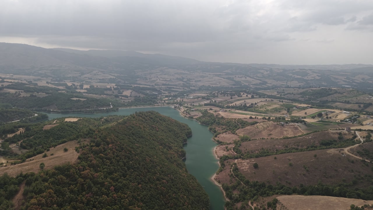 Aerial drone forward shot over the Yalakdere River flowing through green countryside and farmland in Gölcük, Kocaeli, Turkey on a cloudy day.