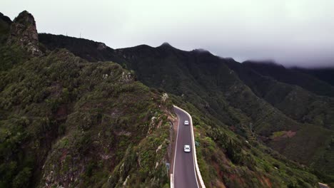 aerial of two cars drive on mountain pass ridge road in green landscape