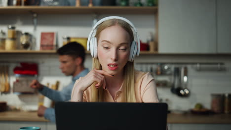una chica entrenadora hablando en videoconferencia en la cocina con auriculares. un chico bailando.