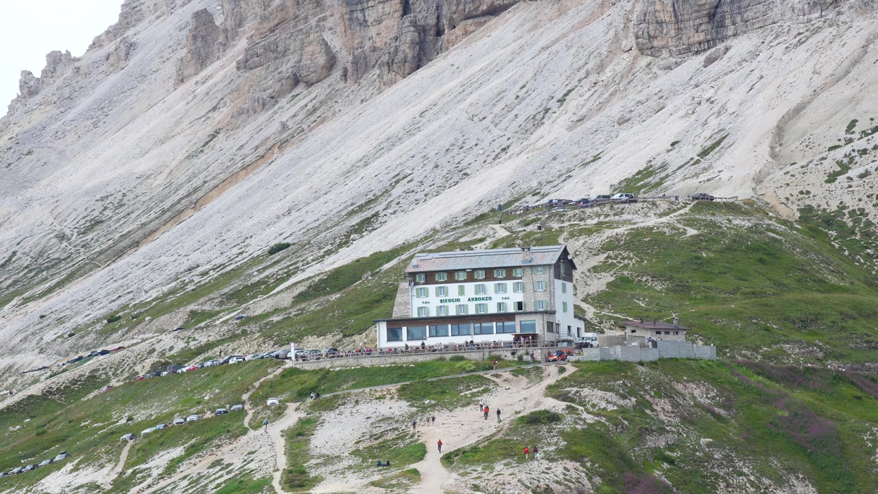 Vista panoramica del Rifugio Auronzo ai piedi delle iconiche vette delle Tre Cime di Lavaredo, circondato da spettacolari paesaggi alpini nelle Dolomiti, Italia.