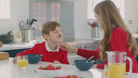 Brother-And-Sister-Wearing-School-Uniform-In-Kitchen-Have-Fun-Hanging-Spoon-From-Noses-At-Breakfast
