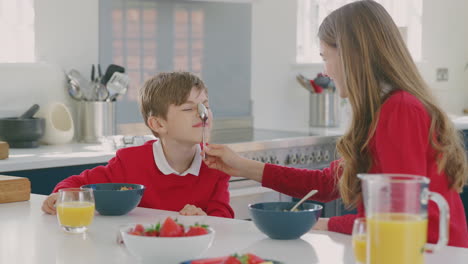 Hermano-Y-Hermana-Vistiendo-Uniforme-Escolar-En-La-Cocina-Se-Divierten-Colgando-Una-Cuchara-De-La-Nariz-En-El-Desayuno