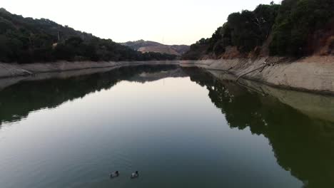 video de avión no tripulado capturando la belleza del embalse de stevens creek en cupertino, california, con dos patos nadando en las aguas reflectantes con el paisaje de la montaña reflejado en el lago