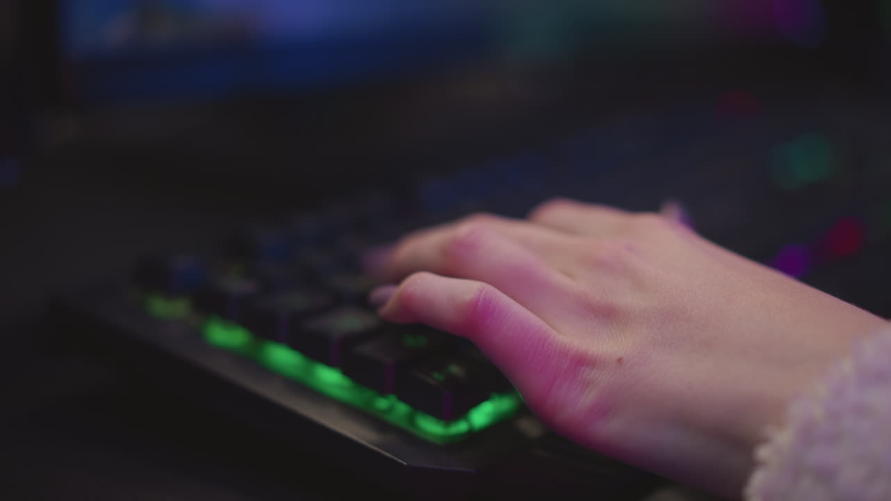 Close up hand view of woman typing on glowing mechanical keyboard with polished nails, surrounded by soft ambient lighting and blurred desktop screen in background