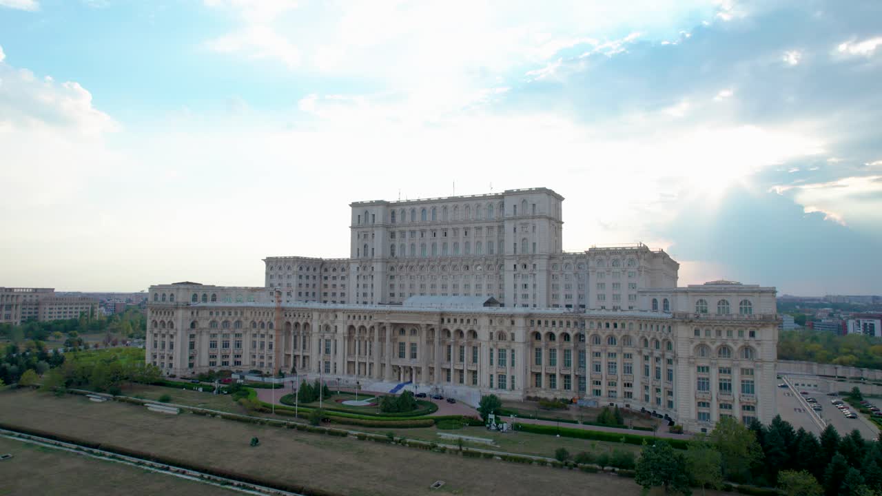 vista giratoria del palacio del parlamento en bucarest, rumania con un cielo azul en el fondo y gruesas nubes blancas y naranjas al atardecer