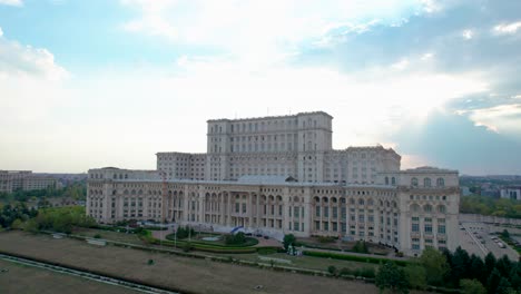 rotating drone view of the palace of parliament in bucharest, romania with a blue sky in the background and thick white and orange clouds at sunset