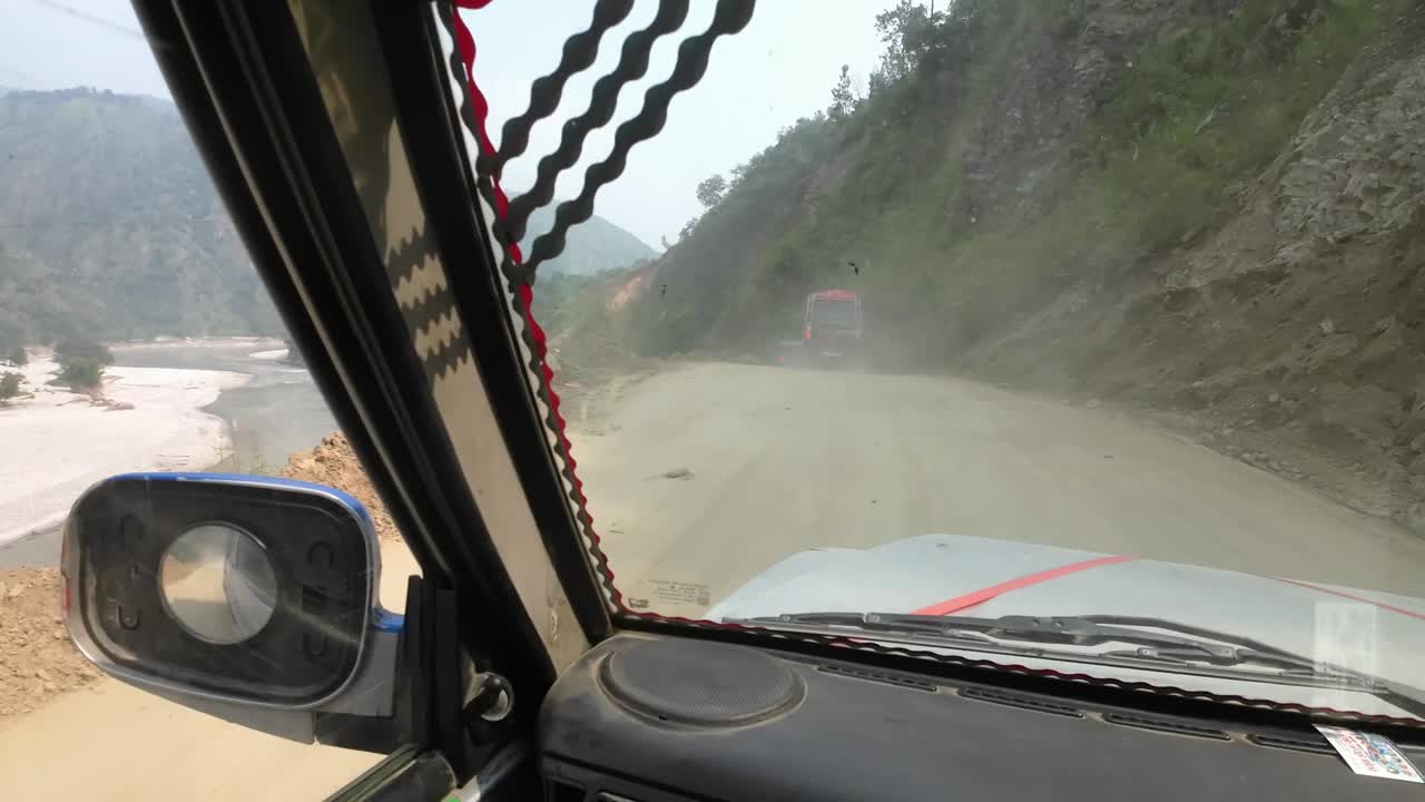 Slow POV jeep ride through Nepal's rugged interior on dusty dirt roads. Other vehicles in front. Next to Sunkoshi River