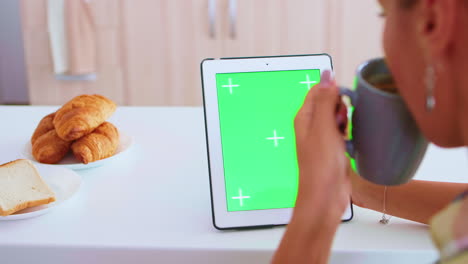 Sitting-at-table-looking-at-tablet-computer-with-green-screen