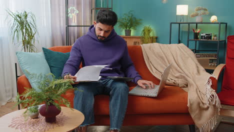 young indian businessman working with laptop computer documents planning expenses budget at home