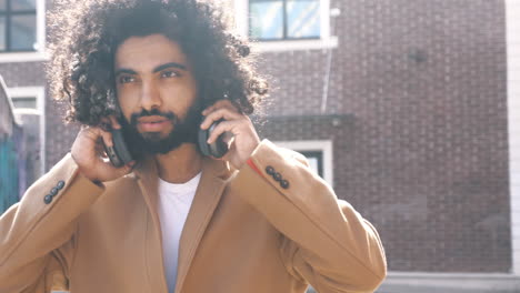man with curly hair and headphones in a cityscape