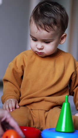 calm peaceful kid sitting on the floor watching his mom putting the toys in front of him. mommy teaching her son colors. blurred backdrop. vertical video