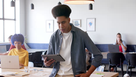 Portrait-of-happy-biracial-male-creative-using-tablet-in-office-with-diverse-colleagues,-slow-motion