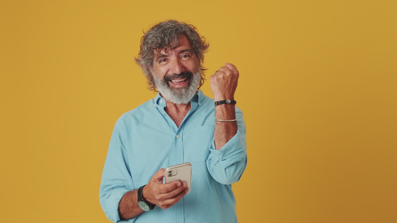 Uomo maturo felice che celebra il successo mentre usa lo smartphone