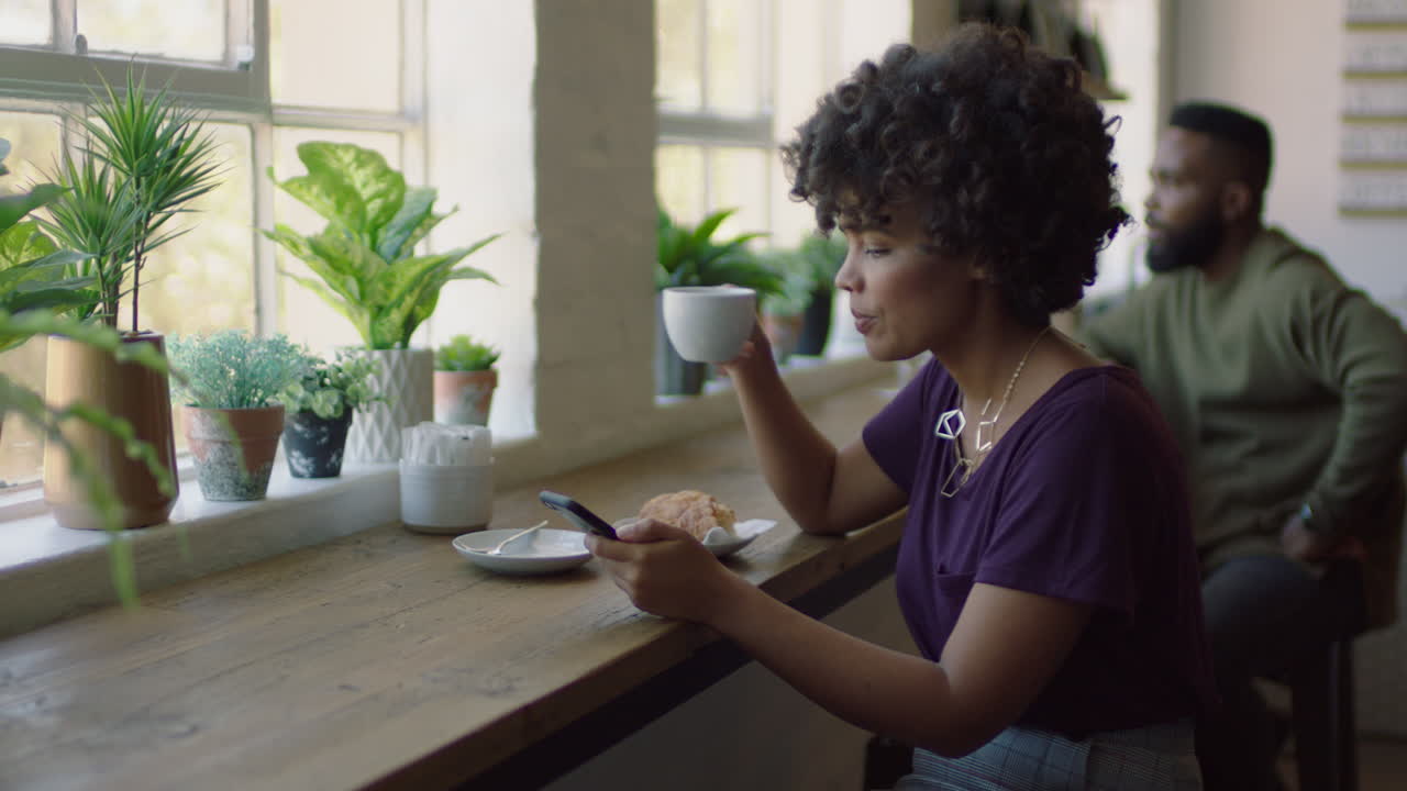 joven mujer afroamericana usando un teléfono inteligente en una cafetería navegando por mensajes en línea bebiendo café elegante mujer negra enviando mensajes de texto compartiendo estilo de vida en las redes sociales disfrutando del teléfono móvil
